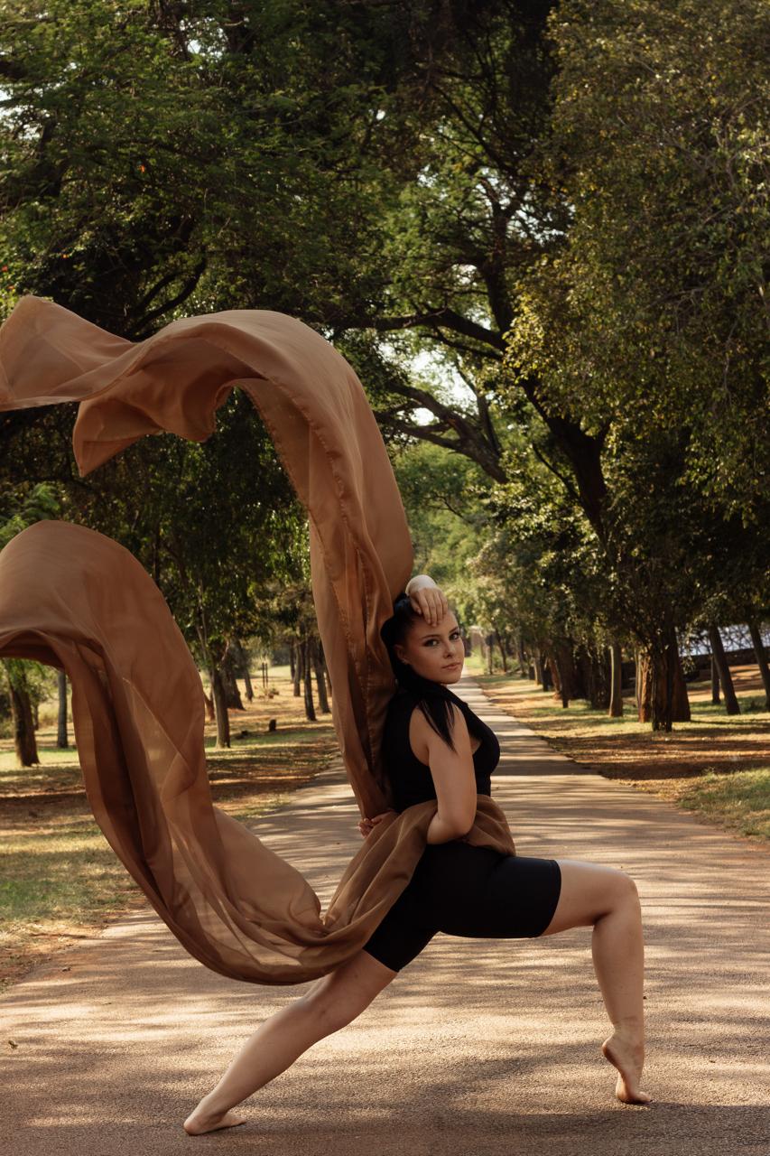 A dancer with flowing copper fabric in a lunge on a tree-lined path