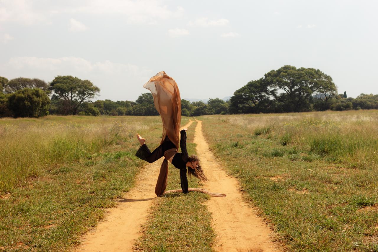 A dancer upside down with flowing fabric on a dirt track